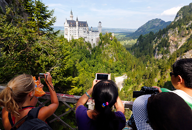 Туристы фотографируют замок на фоне гор