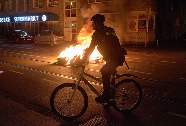 Полицейский на велосипеде возле горящего мусорного бака в Гааге