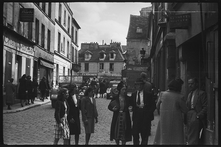 Немецкие военные на автомобиле и пешие местные жители на одной из улиц города в районе Монмартра. Париж, Франция, 1940 год.
