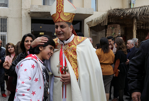 Священник обнимает девочку-христианку после мессы в Багдаде