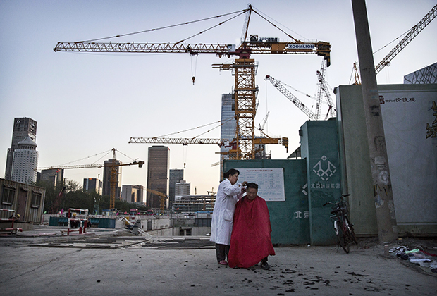 Парикмахерша стрижет рабочего-мигранта на строительной площадке, Пекин, 2014 год