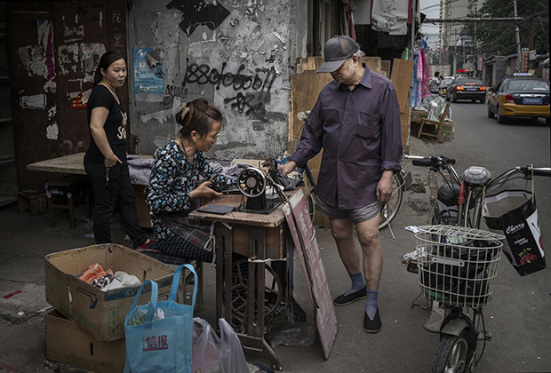 Китаец из бедного района стоит в трусах, пока портниха зашивает ему штаны, Пекин, 2015 год