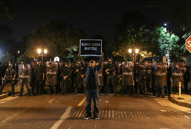 Участник акции протеста с плакатом «Жизни черных важны» позирует на фоне полицейских в Сент-Луисе, штат Миссури