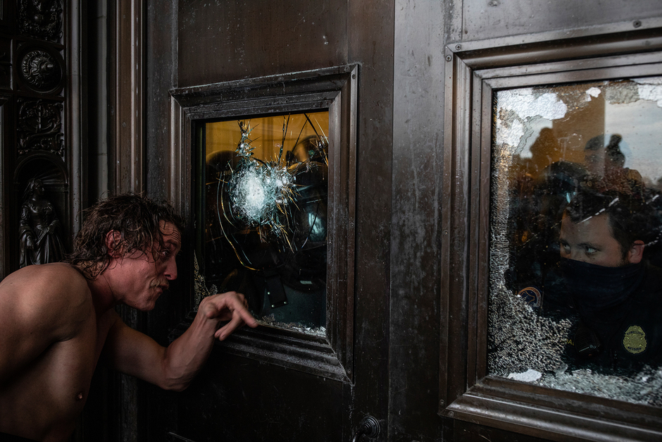 Этот снимок иллюстрирует, как полуголый мужчина — один из сторонников бывшего президента США Дональда Трампа — старается проникнуть в здание Капитолия. Он попытался разбить окно, чтобы открыть дверь, но внутри его уже ждут вооруженные полицейские.
