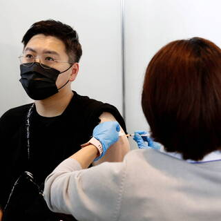 Мужчине делают прививку в Токио