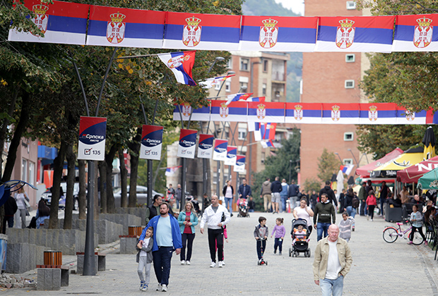 Люди идут по улице, украшенной сербскими флагами, в Косовска-Митровице