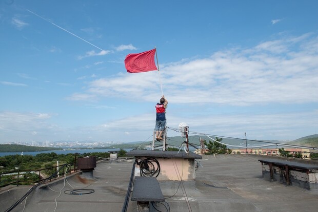 Анатолий Жегель закрепляет флаг на своем доме в поселке Подножье на острове Русский. Фото: Антон Новгородов
