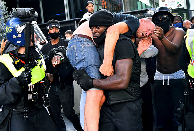 Протестующий Патрик Хатчинсон несет раненого демонстранта в безопасное место во время протестов в Лондоне