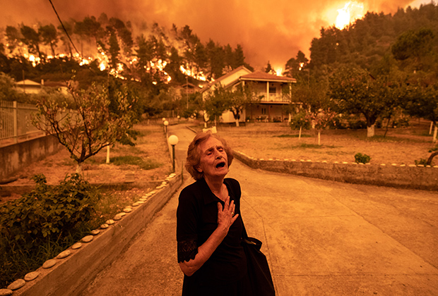 Пожилая дама покидает свой дом, которому угрожает лесной пожар, в деревне Гувес на острове Эвия, Греция 