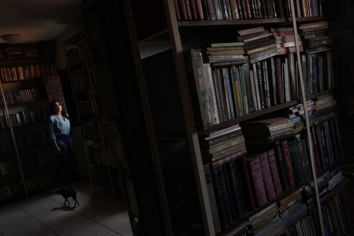 Присцила Баррос позирует для фотографии в библиотеке, которую ее отец оставил в доме в районе Пиньейру. Баррос отказывается покидать свой дом, в котором живет более 30 лет