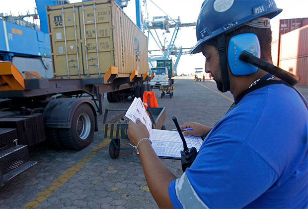 Рабочий регистрирует погрузку контейнера на грузовое судно 