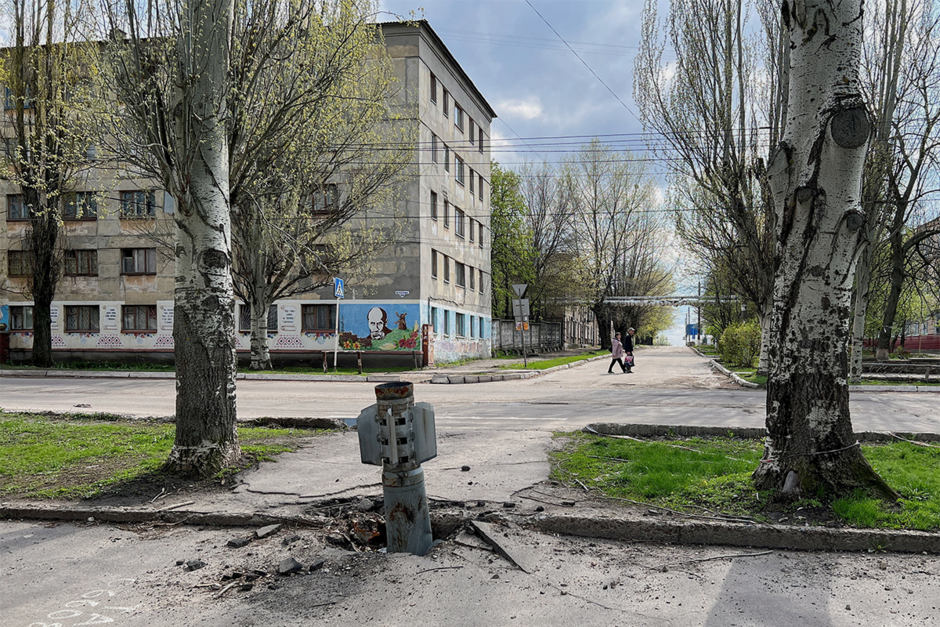 Люди идут по улице мимо застрявшей в земле ракеты в Рубежном, 21 апреля 2022 года