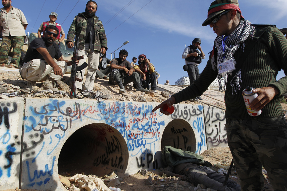 Повстанец показывает дренажный канал, где нашли раненого Каддафи