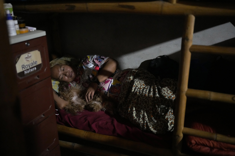 Квин Пангке Табора лежит в постели со своей собакой Чокнут в их комнате в лагере Ocean Camp, май 2022 года