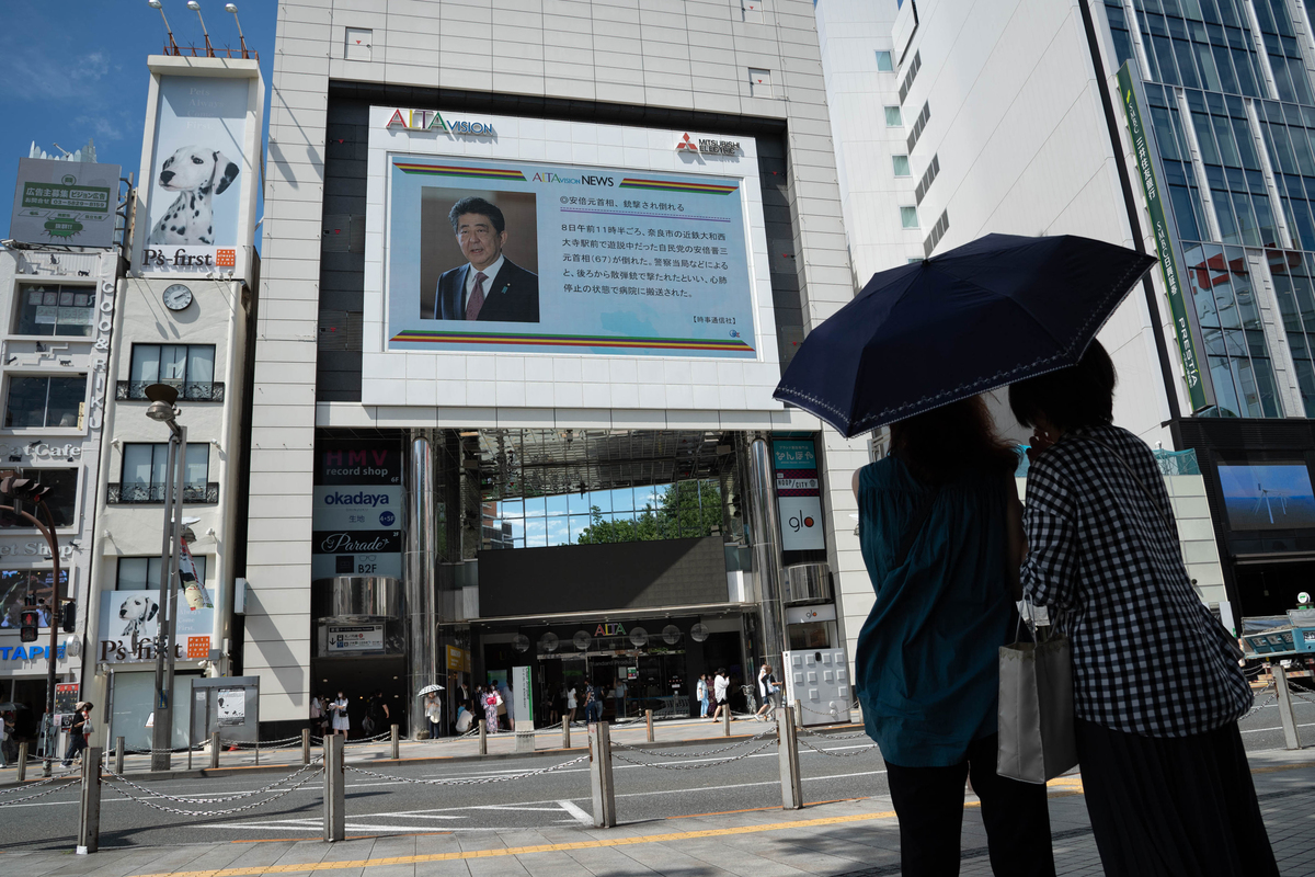 Прохожие читают сообщение на уличном экране в Токио о смерти Абэ