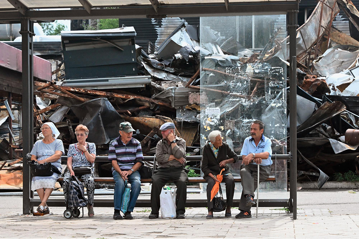 Жители Мариуполя на остановке городского транспорта на фоне разрушенного дома.