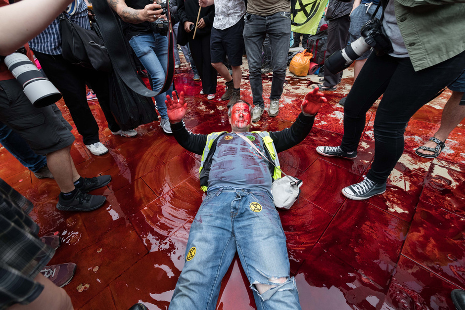 Активист Extinction Rebellion лежит в напоминающей кровь жидкости на площади в Лондоне