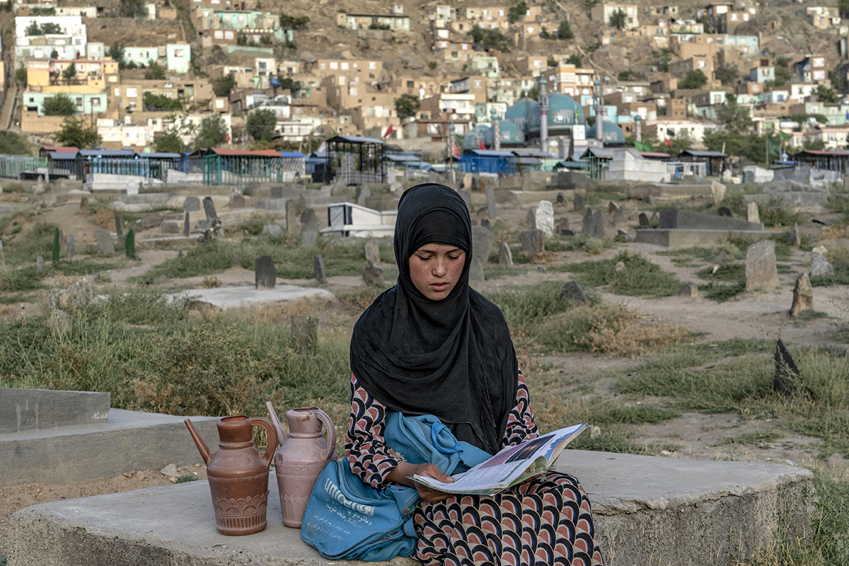 14-летняя афганская девочка Сара на кладбище в ожидании покупателей воды читает книгу, Кабул, Афганистан, 30 июля 2022 года