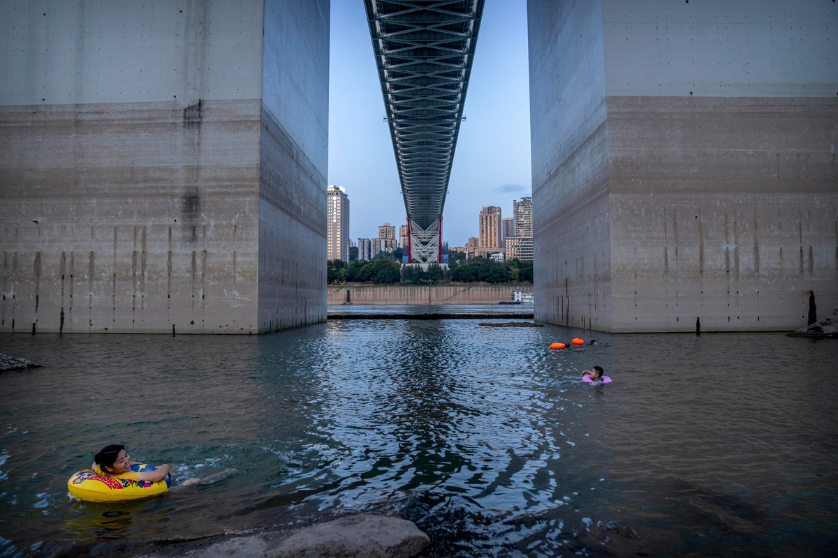 Люди плавают в реке Янцзы около опорных столбов моста в муниципалитете Чунцин