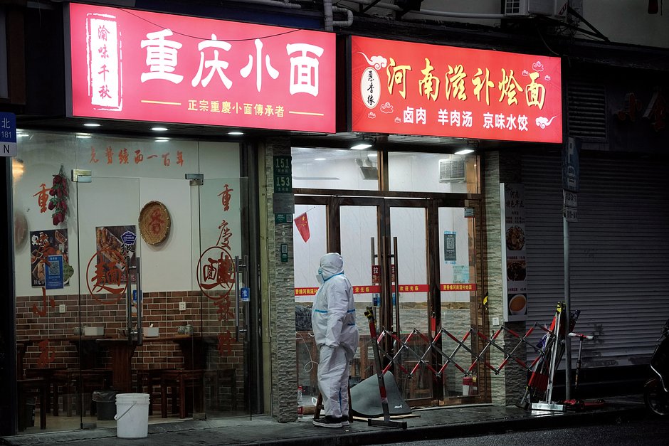 Человек в защитном костюме возле магазинов лапши во время вспышки COVID-19 в Шанхае, 30 ноября 2022 года