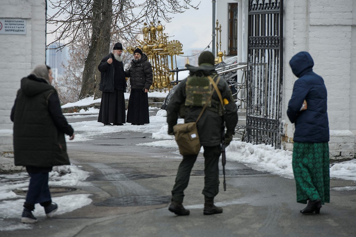Православные священники смотрят на сотрудника правоохранительных органов на территории монастыря Киево-Печерской лавры, 22 ноября 2022 года