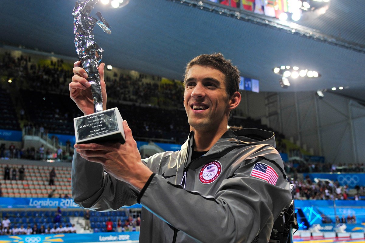 Майкл Фелпс улыбается и держит в руках награду, полученную во время Олимпийских игр 2012 года в Лондоне 