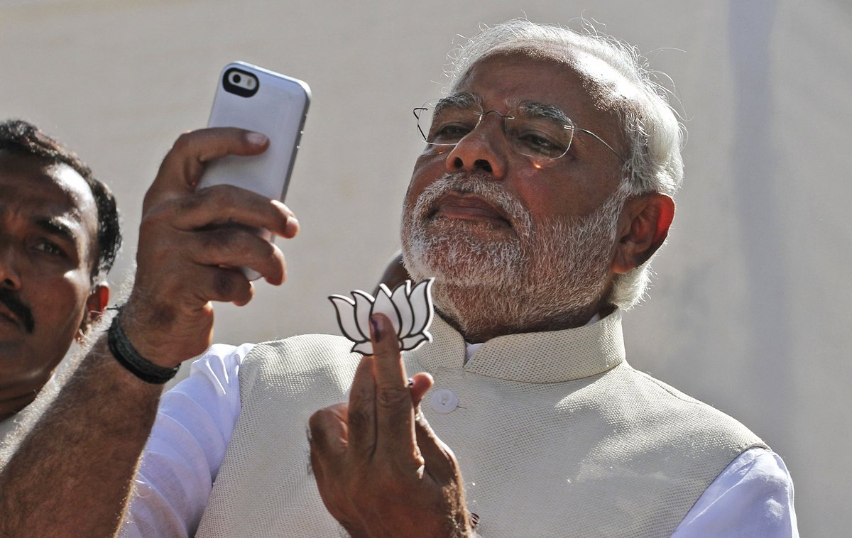 На фотографии, сделанной 30 апреля 2014 года, тогдашний кандидат в премьер-министры от основной оппозиционной партии Индии Бхаратия джаната Нарендра Моди держит партийный символ и смотрит в свой телефон после голосования в Ахмадабаде, Индия