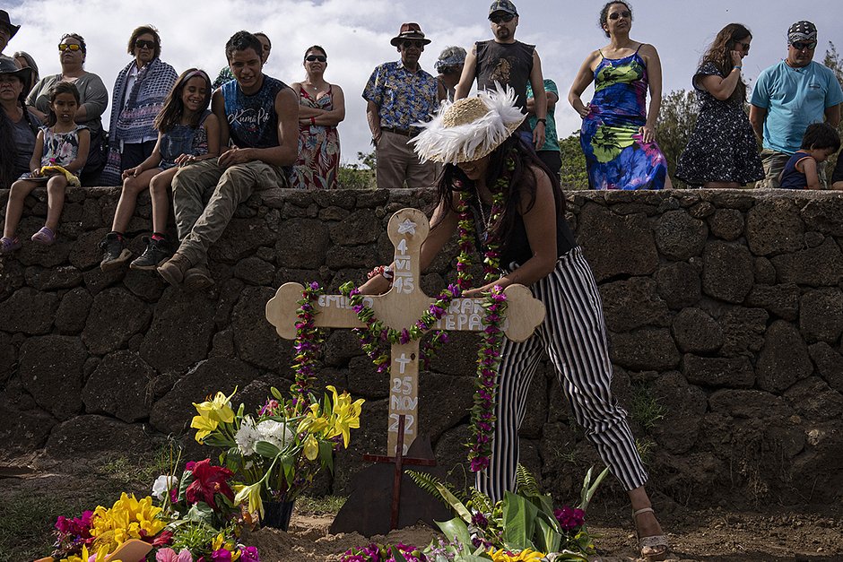 Местный житель возлагает ожерелье из цветов на могилу коневода и бывшего военного водолаза Эмилио Араки во время его похорон на кладбище Анга-Роа