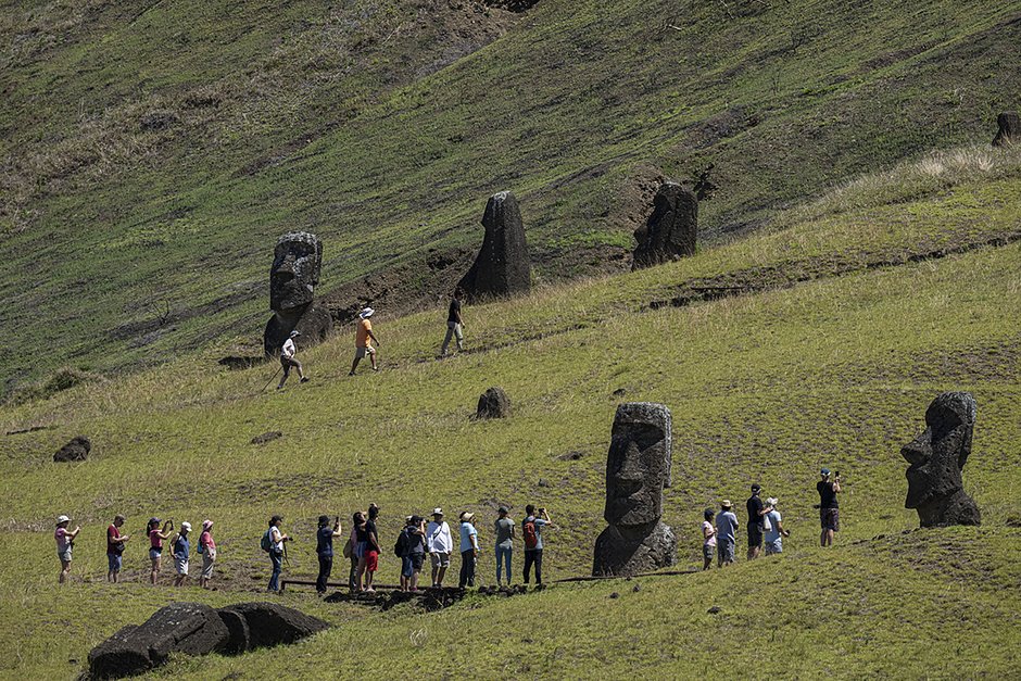 Туристы фотографируются на фоне статуй моаи на склонах вулкана Рано-Рараку