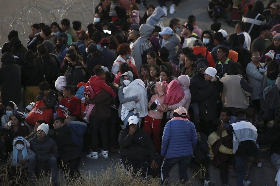 Мигранты стоят за колючей проволокой, преграждающей их путь к Эль-Пасо, 20 декабря 2022 года