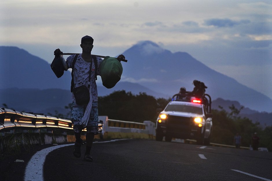 Мигрант идет по шоссе, за ним следует автомобиль мексиканской национальной гвардии, Хуикстла, штат Чьяпас, Мексика, 9 июня 2022 года