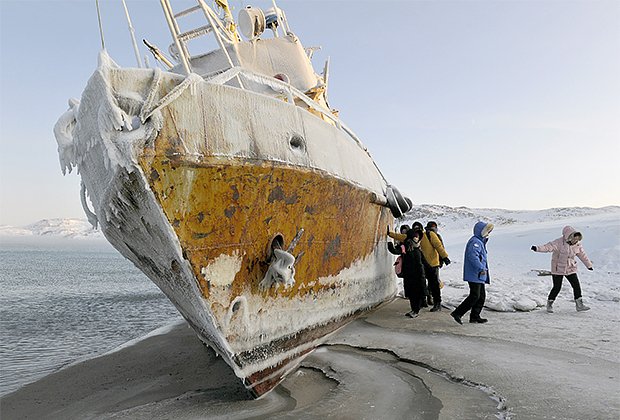 Китайские туристы на фоне рыбацкого судна, выброшенного на берег в бухте Лодейная