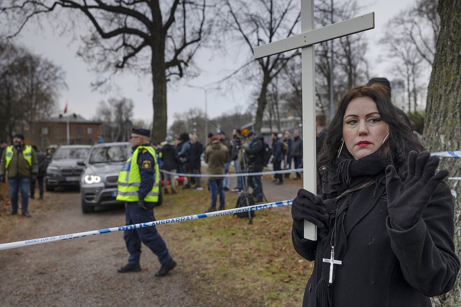 Женщина держит крест, пока Расмус Палудан сжигает Коран у посольства Турции в Стокгольме, Швеция, 21 января 2023 года