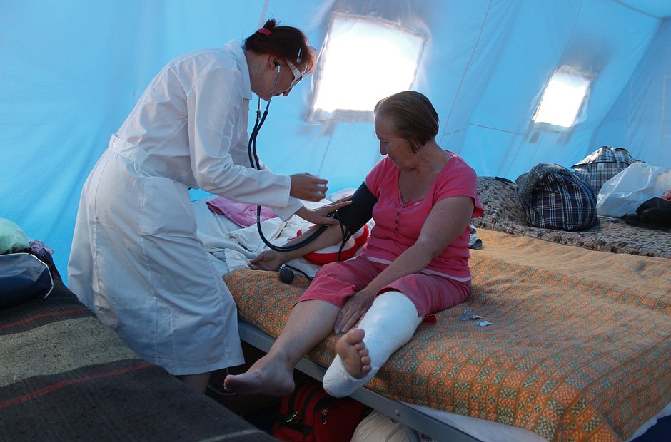 Врач измеряет давление женщине-беженке в палаточном лагере для вынужденных переселенцев из Донбасса