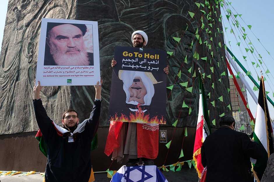 Демонстрант с фотографией аятоллы Хомейни рядом со священнослужителем, в руках у которого флаг Ирана и перевернутое знамя короля Саудовской Аравии Салмана бин Абдулазиза. 39-я годовщина Исламской революции, 11 февраля 2018 года, Тегеран, Иран