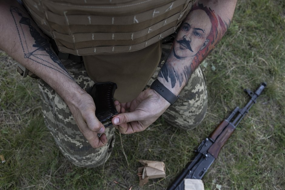 Мужчина с татуировкой, изображающей британского преступника, известного как «Чарльз Бронсон», перезаряжает оружие во время учений полка «Азов» в Харьковской области, 28 июня 2022 года