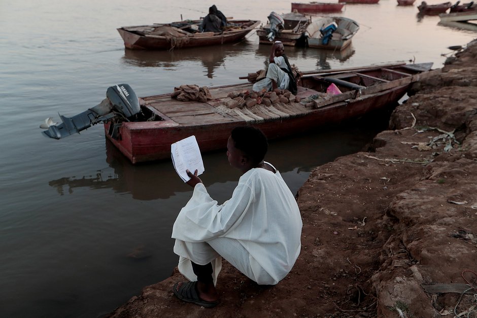 Ученик старшей школы читает конспекты, сидя на берегу реки Нил в Алкамайире, Омдурман, Судан, 15 февраля 2020 года