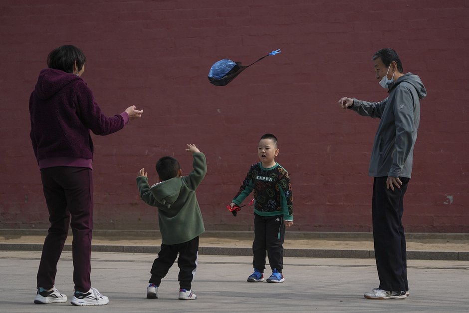 Жители Пекина в медицинских масках гуляют с детьми. 19 марта 2023 года
