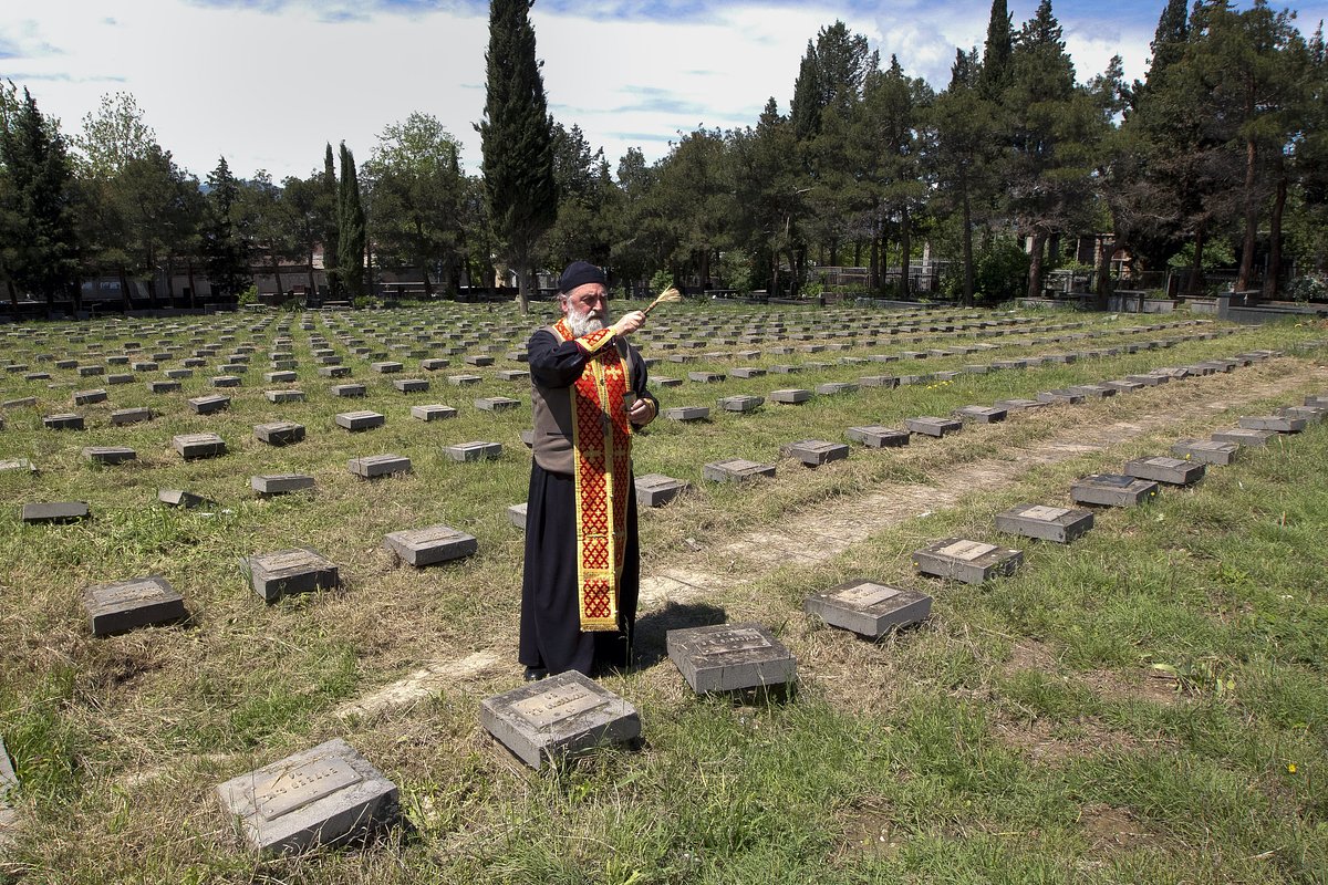 Православный священник освящает могилы на военном кладбище в Тбилиси, Грузия, 9 мая 2022 года