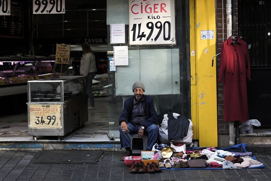 Пожилой уличный торговец одеждой рядом с мясным магазином на открытом рынке в районе Фатих в Стамбуле, Турция, 23 мая 2023 года