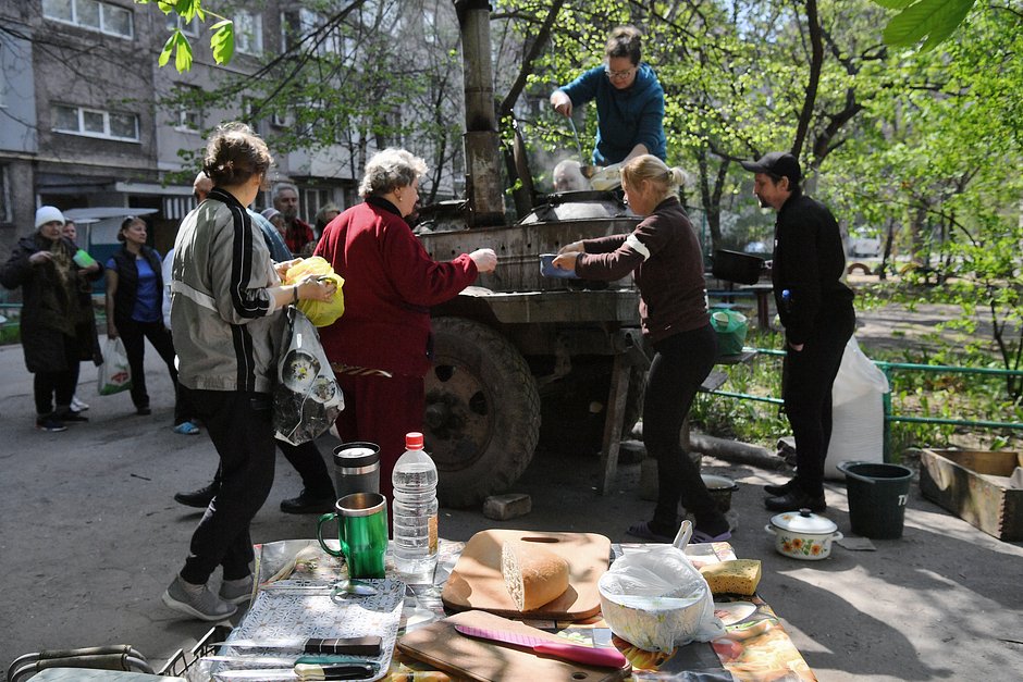 Местные жители готовят еду в полевой кухне, которую доставили им волонтеры, во дворе разрушенного дома в Левобережном районе Мариуполя, 29 апреля 2022 года