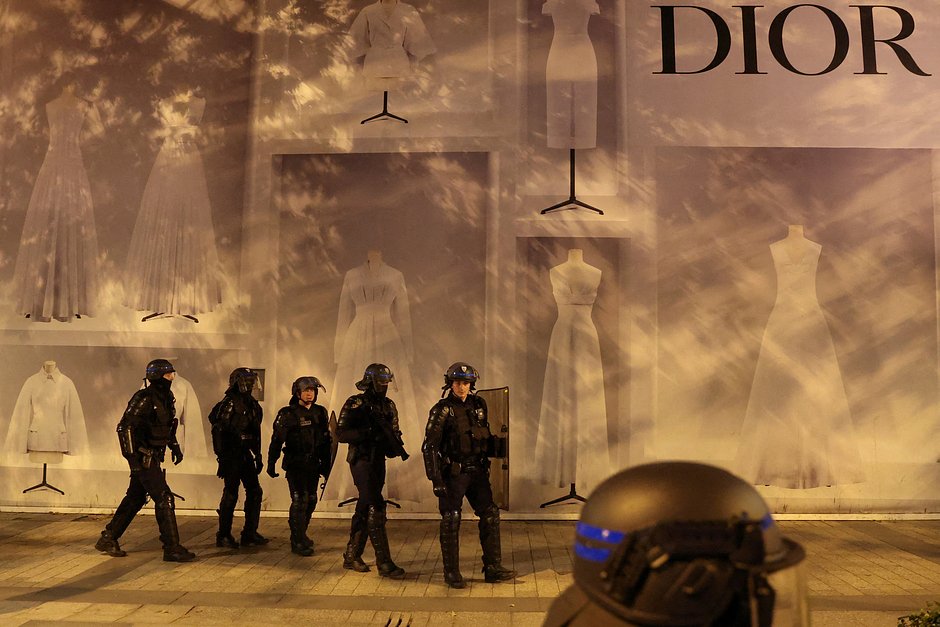 Полицейские охраняют витрину перед зданием магазина Dior во время беспорядков на Елисейских Полях, Париж, Франция, 1 июля 2023 года
