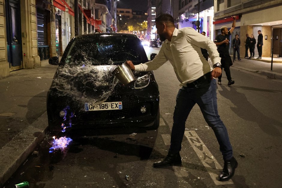 Мужчина льет воду, чтобы потушить подожженную в ходе беспорядков машину, Париж, Франция, 2 июля 2023 года