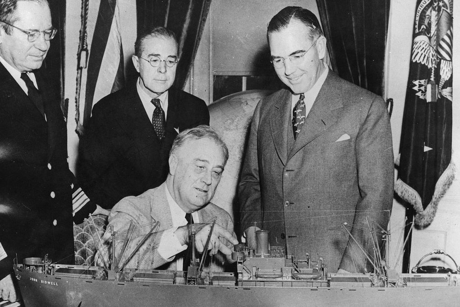 Президент США Франклин Рузвельт (сидит) в Белом доме осматривает модель нового транспортного корабля Liberty, 25 января 1943 года