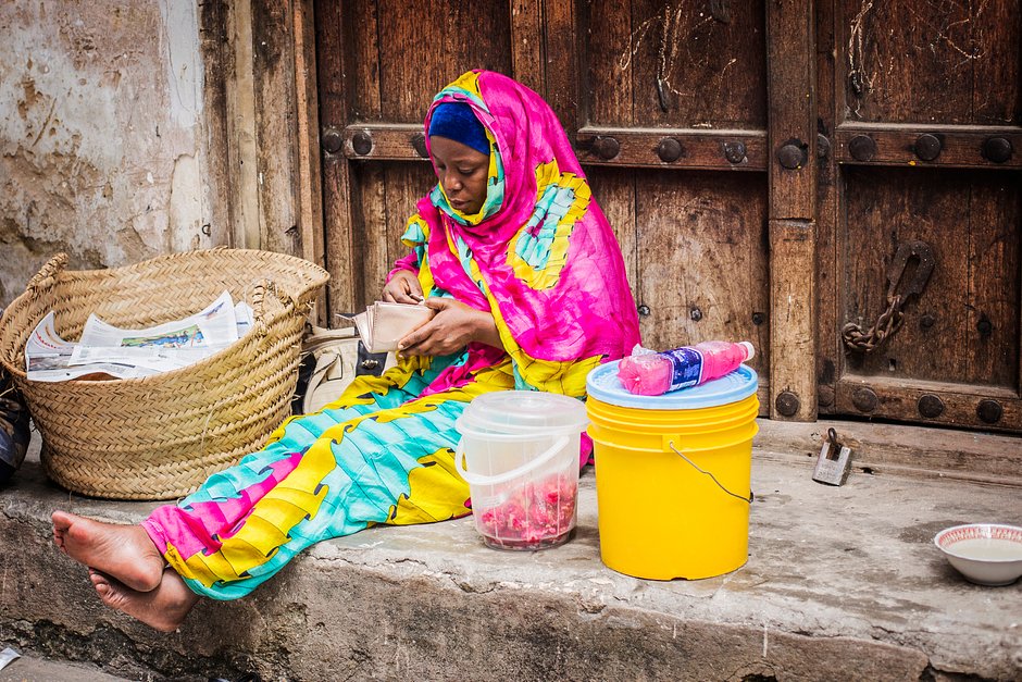 Африканка, одетая в яркий мусульманский наряд, продает фрукты на рынке в Стоун-Тауне