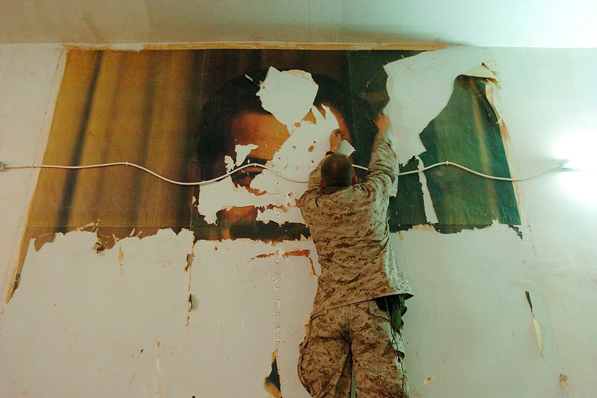 Американский морской пехотинец снимает плакат с изображением Саддама Хусейна со стены во время подготовки к военному наступлению против иракских повстанцев в городе Фаллуджа, Ирак, 3 ноября 2004 года