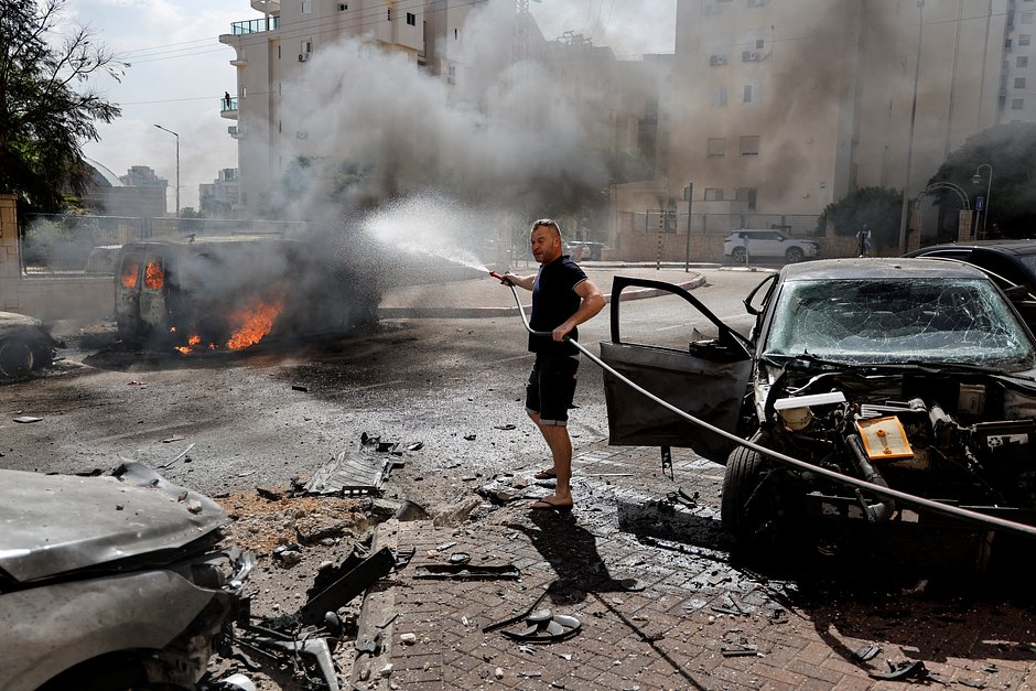 Мужчина тушит горящий фургон после ракетного удара по Ашкелону, на юге Израиля, 7 октября 2023 года