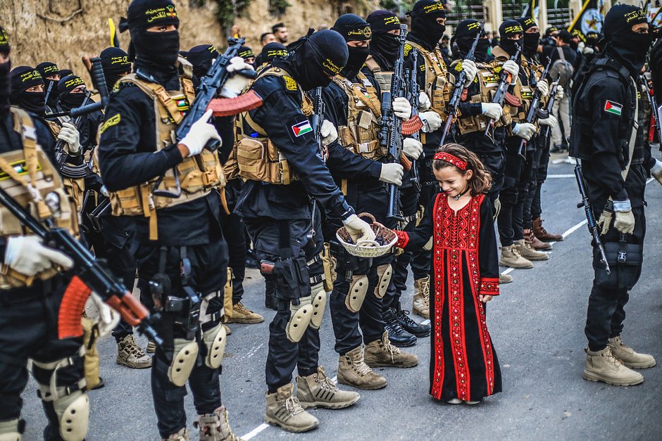 Палестинская девочка раздает сладости вооруженным бойцам из бригад Аль-Кудс, военного крыла движения «Исламский джихад» в Палестине, во время военного парада, посвященного 36-й годовщине основания движения на юге сектора Газа, 10 апреля 2023 года