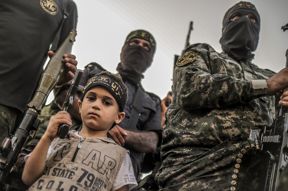 Палестинский ребенок среди вооруженных бойцов Сарайя аль-Кудс, военного крыла «Исламского джихада», во время антиизраильского военного парада, посвященного 35-й годовщине создания движения в лагере беженцев Джабалия на севере сектора Газа, 3 октября 2022 года