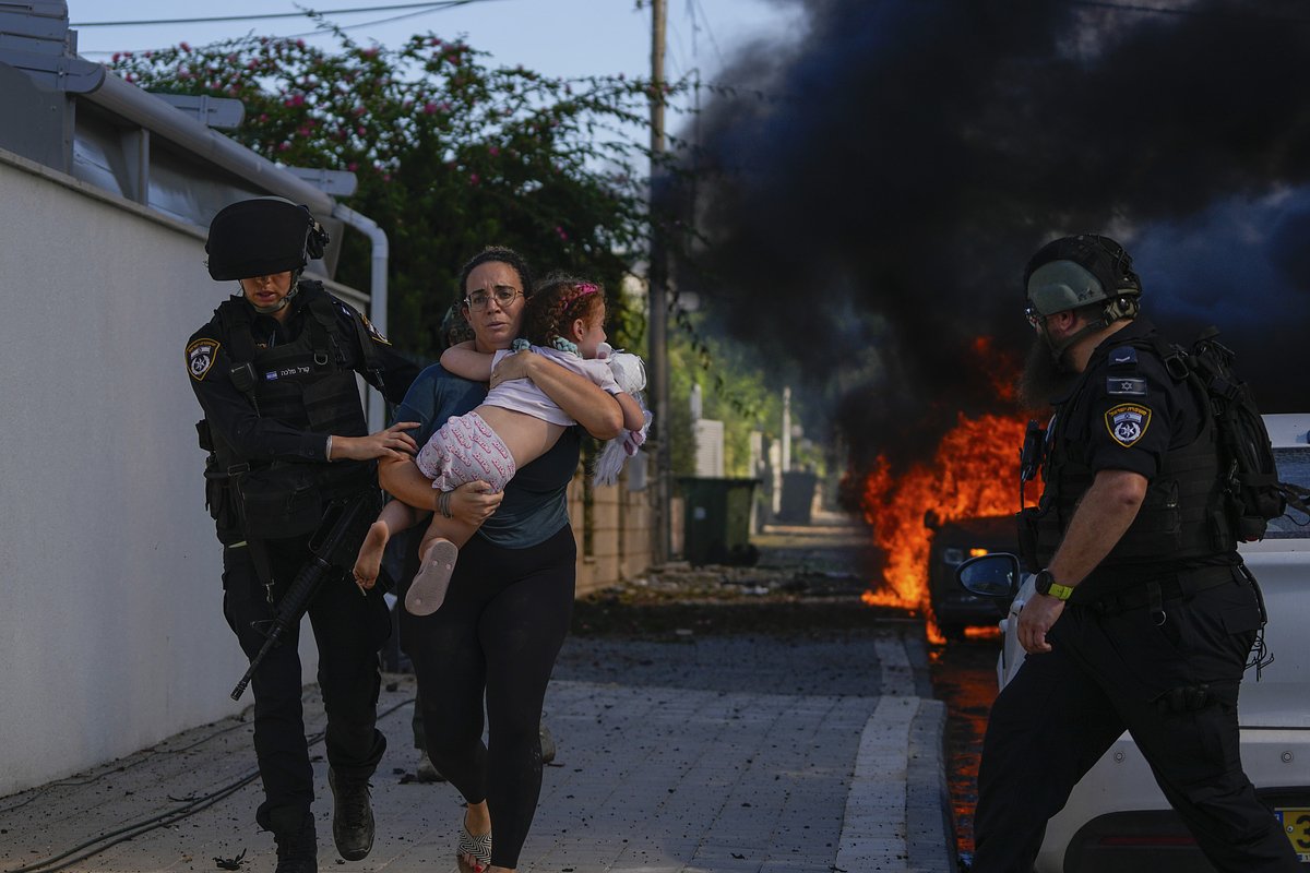 Израильские полицейские помогают женщине с ребенком эвакуироваться из дома, в который попала выпущенная из сектора Газа ракета, 7 октября 2023 года